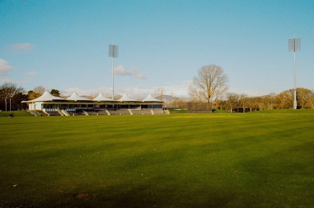 Empty sports field beside a small stadium grandstand and floodlights
