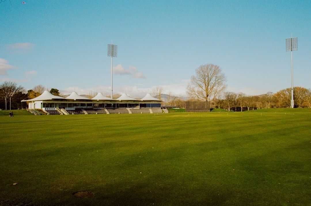 Empty sports field beside a small stadium grandstand and floodlights