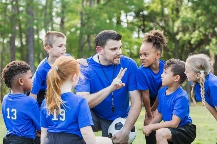 Youth soccer coach speaking with children during an outdoor team practice